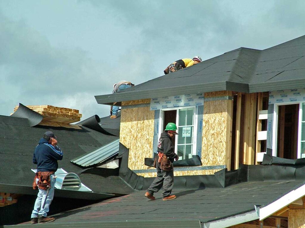 A home with a visible roof, attic venting, and mature trees in a quiet neighborhood after a seasonal change.
